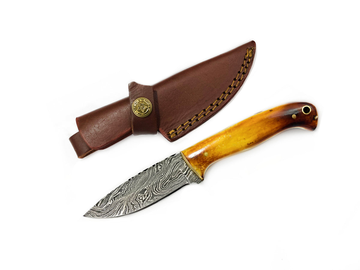 Damascus Hunting Knife with burnt bone handle and brass pins resting on wooden surface