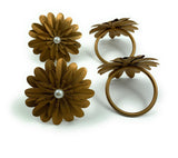 Set of four golden metal napkin rings shaped like layered flowers with small white pearl centers, displayed on a white background in two facing pairs.