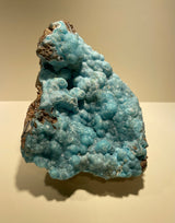 Botryoidal blue hemimorphite specimen with rounded bubbly formations and patches of brown matrix, shown against a soft beige background.