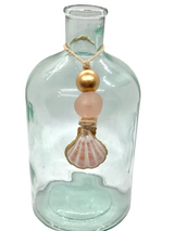 Clear glass bottle decorated with a twine necklace featuring a gold bead, a blush pink frosted bead, and a small pink scallop shell pendant.