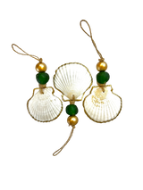 Three white scallop shells edged in gold, each adorned with green and gold beads on jute cord loops against a black background.