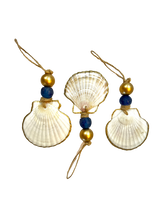 Three white scallop shell ornaments with gold and blue beads threaded on natural twine loops, arranged on a black background