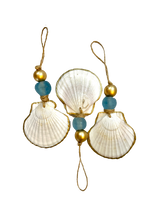 Three white scallop shell ornaments edged with gold paint, each adorned with a blue bead and two gold spherical beads, hanging from natural twine loops.