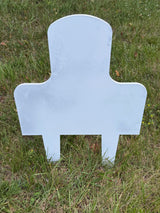 White steel battle rifle target shaped with a rounded top and broad shoulders, standing upright on green grassy ground outdoors.