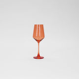 Translucent orange wine glass with a faceted bowl and slender stem standing against a plain white background.