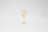Tall wine glass with a lemon yellow tint, featuring a thin stem and a faceted bowl that narrows slightly at the rim, shown against a plain white background.