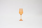 Single translucent orange wine glass with a slender stem placed against a plain white background