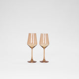 Two amber-colored wine glasses with tall stems and angular bowls standing side by side on a plain white background.