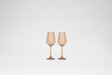 Two stemless wine glasses in a translucent warm brown color, shown upright on a plain white background with soft reflections.