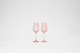 Two stemmed wine glasses in translucent pink, positioned side by side against a plain white background.