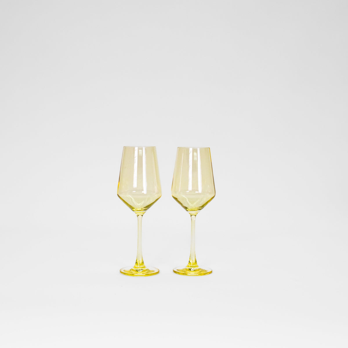 Two lemon-yellow tinted wine glasses with hexagonal bowl shapes and slender stems, shown side by side on a white background.