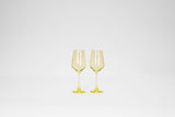 Two lemon drop yellow stemless wine glasses side by side on a plain white background, showing transparent bowl and slender stem with round base.