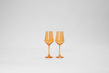 Two translucent orange stemmed wine glasses with a modern angular bowl shape, shown side by side against a plain gray background.