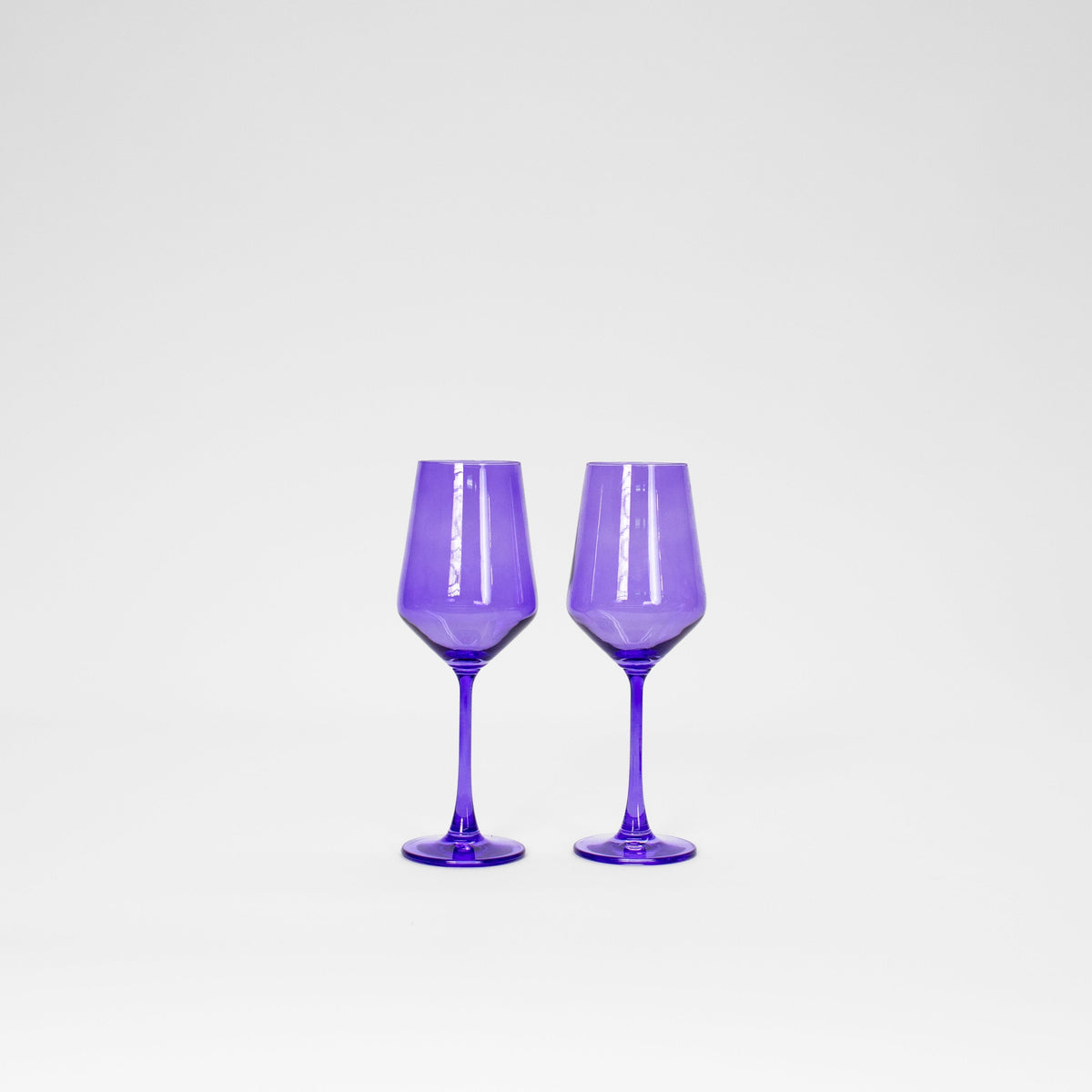 Pair of translucent Veri Peri purple wine glasses with faceted bowl shapes and slender stems, shown side by side on a plain white background.