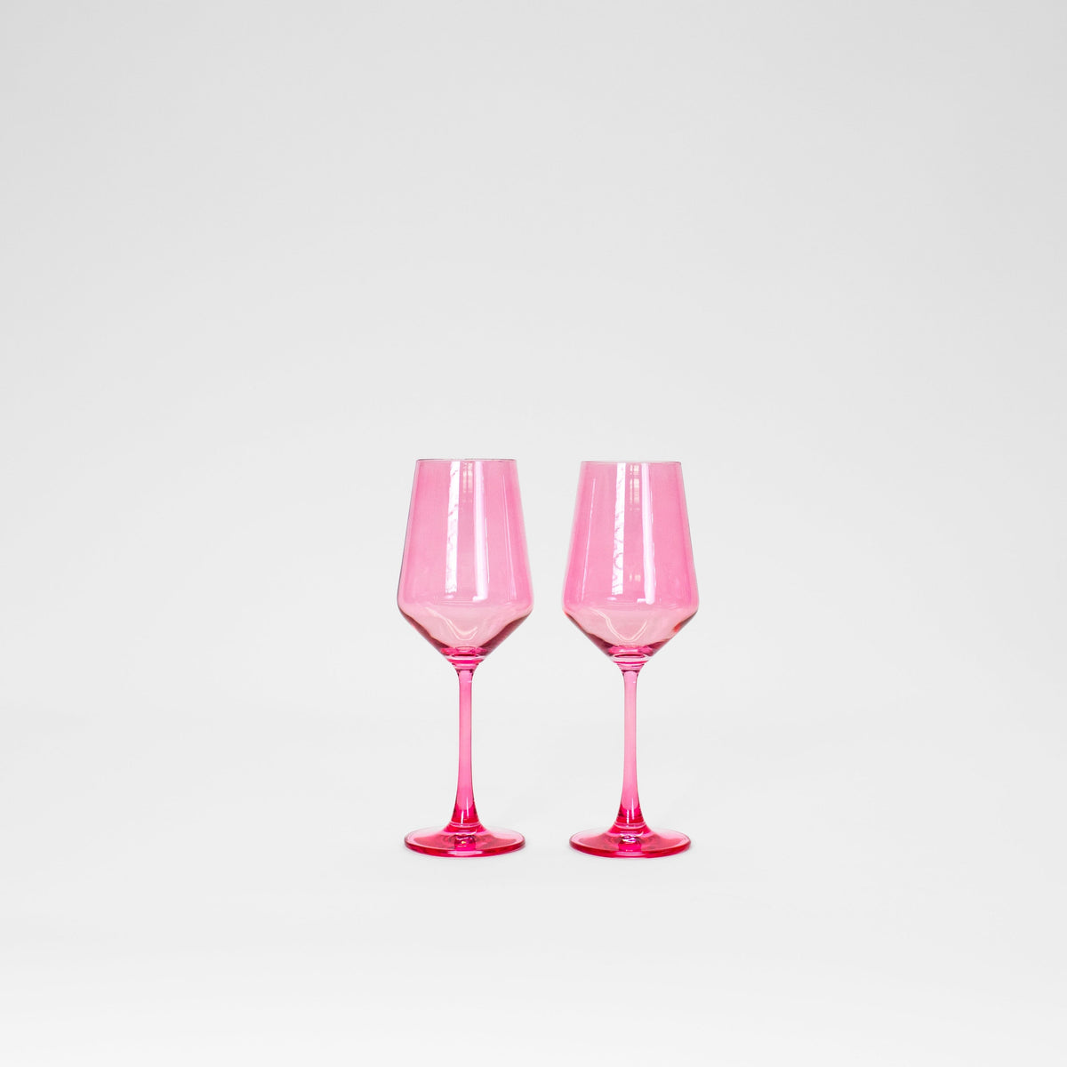 Two translucent bubblegum pink wine glasses with faceted bowls and slender stems, standing side by side on a white background.