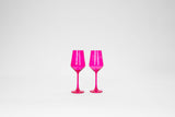 Two vibrant hot pink stemmed wine glasses standing side by side against a plain white background, highlighting their translucent color and elegant shape.