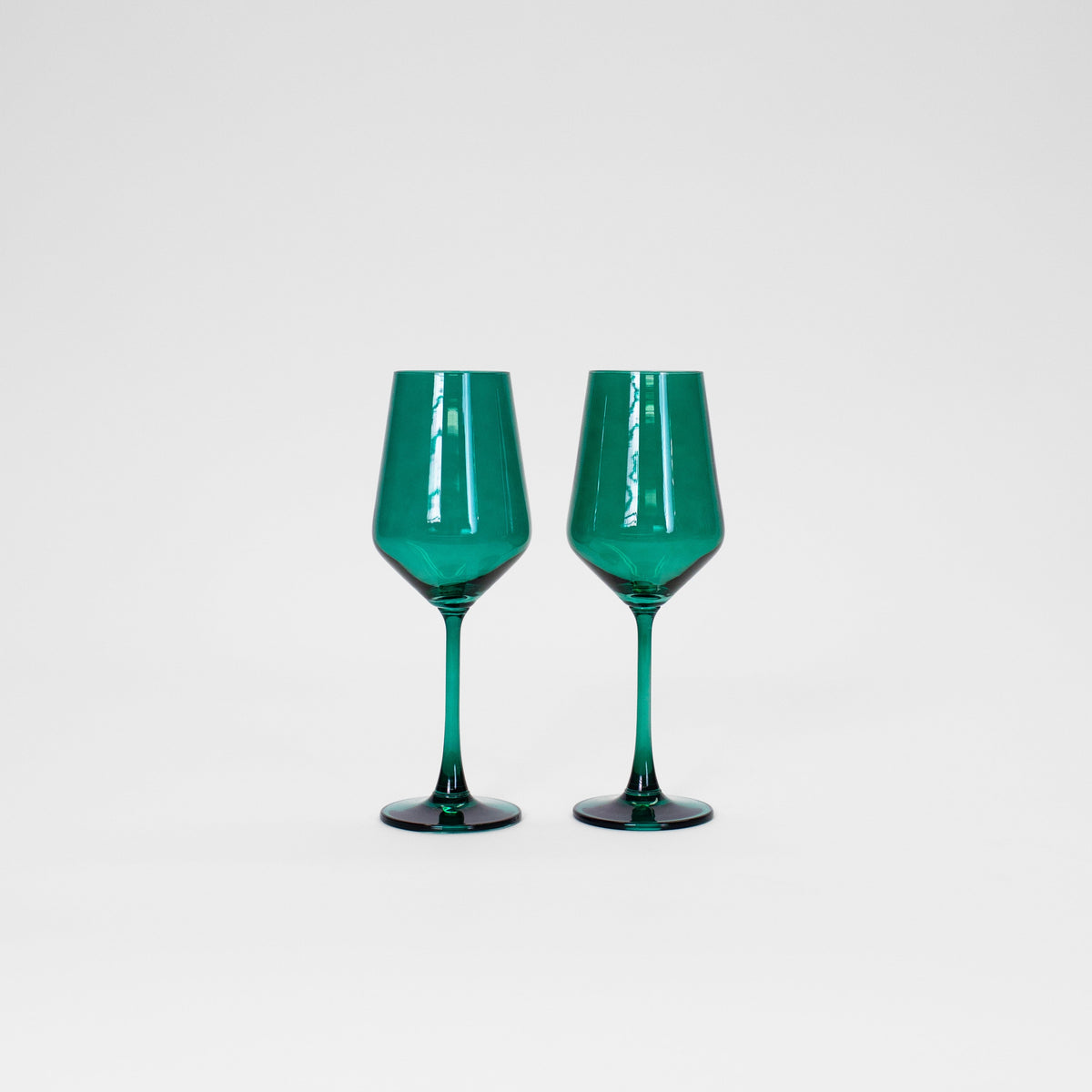 Two emerald green colored wine glasses with faceted bowl design and slender stems, standing side by side on a white surface against a plain background.