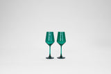 Two emerald green stemless wine glasses with long slender stems and faceted bowls, set against a plain white background.