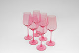 Six bubblegum pink tinted wine glasses grouped on a white surface, each with long stems and rounded bowls, casting soft shadows beneath.