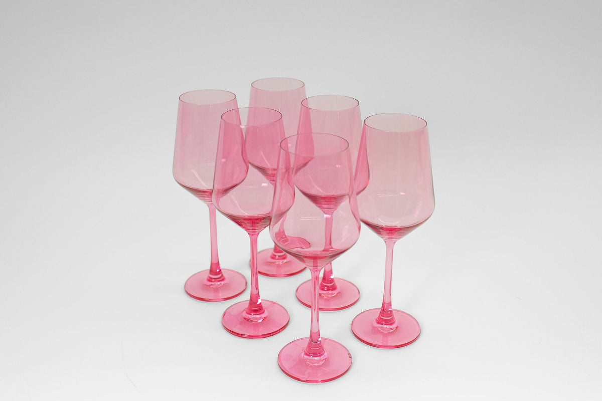 Six bubblegum pink tinted wine glasses grouped on a white surface, each with long stems and rounded bowls, casting soft shadows beneath.