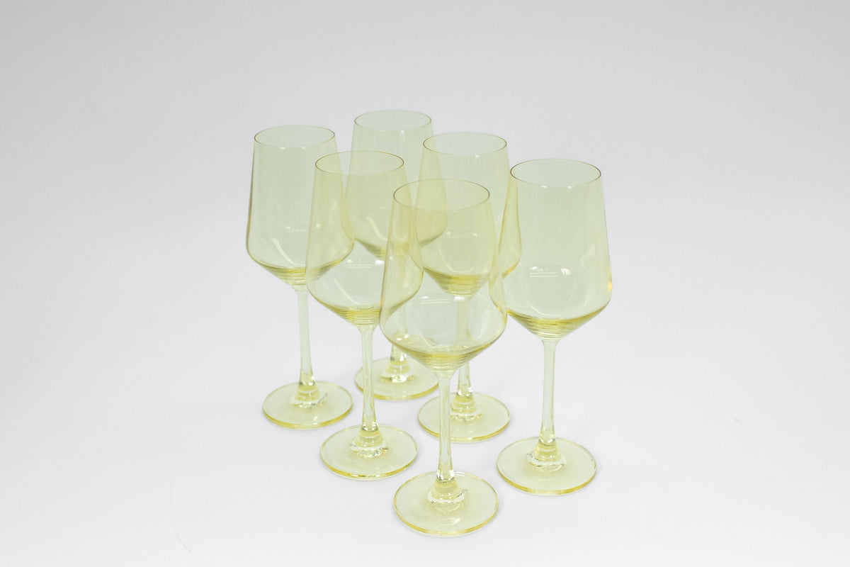 Six pale yellow-tinted wine glasses grouped closely on a white background with long stems and tapered bowls.