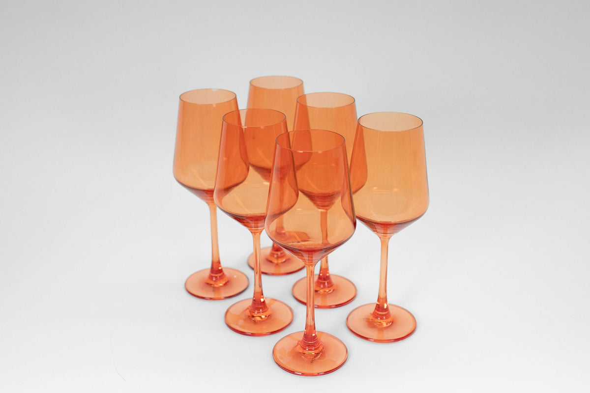 Six orange translucent wine glasses with long stems, arranged in a triangular cluster on a white background.