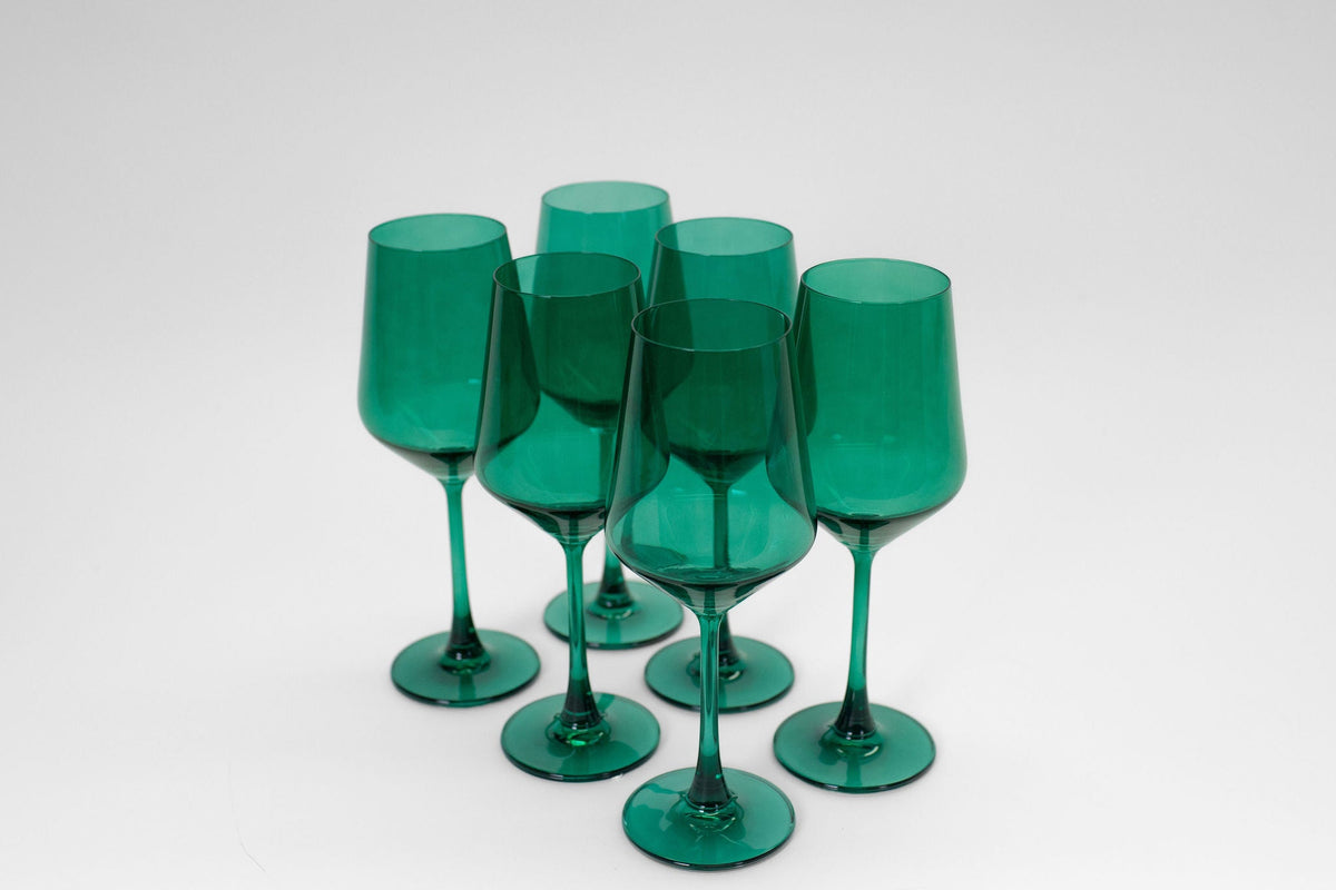 Six emerald green wine glasses with tall stems and rounded bowls, arranged close together on a white background