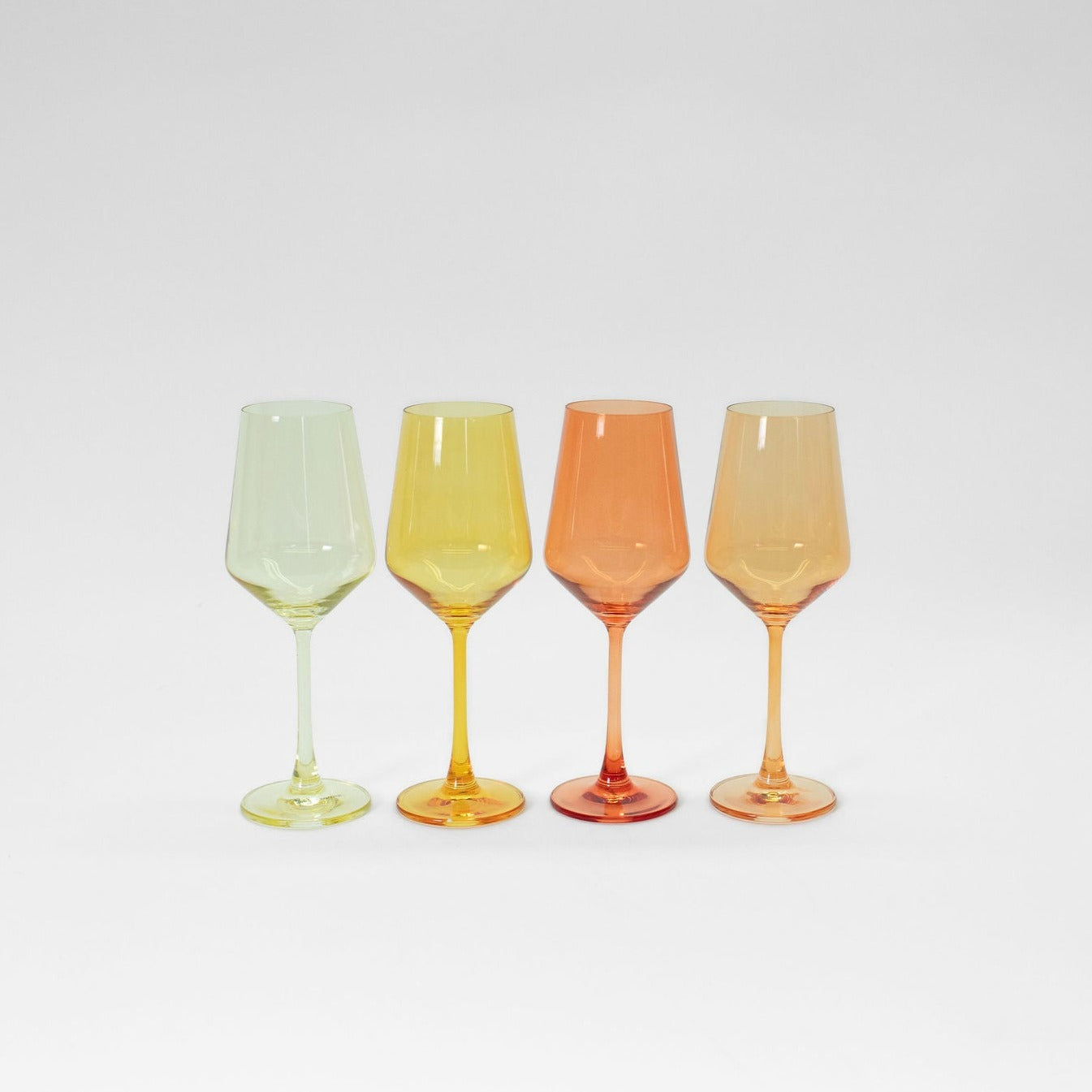 Four colored ombré stemmed wine glasses in yellow, orange, and cream tones arranged on a table