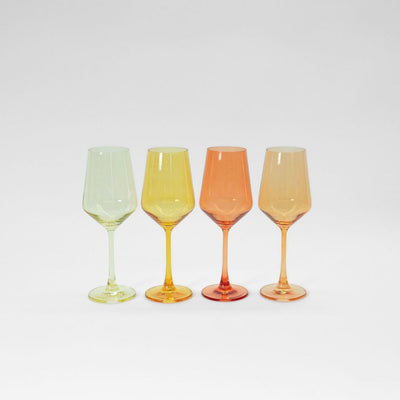 Four colored ombré stemmed wine glasses in yellow, orange, and cream tones arranged on a table
