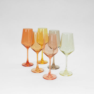 Set of six ombré colored wine glasses with warm shades of yellow, orange, and pink on a table setting