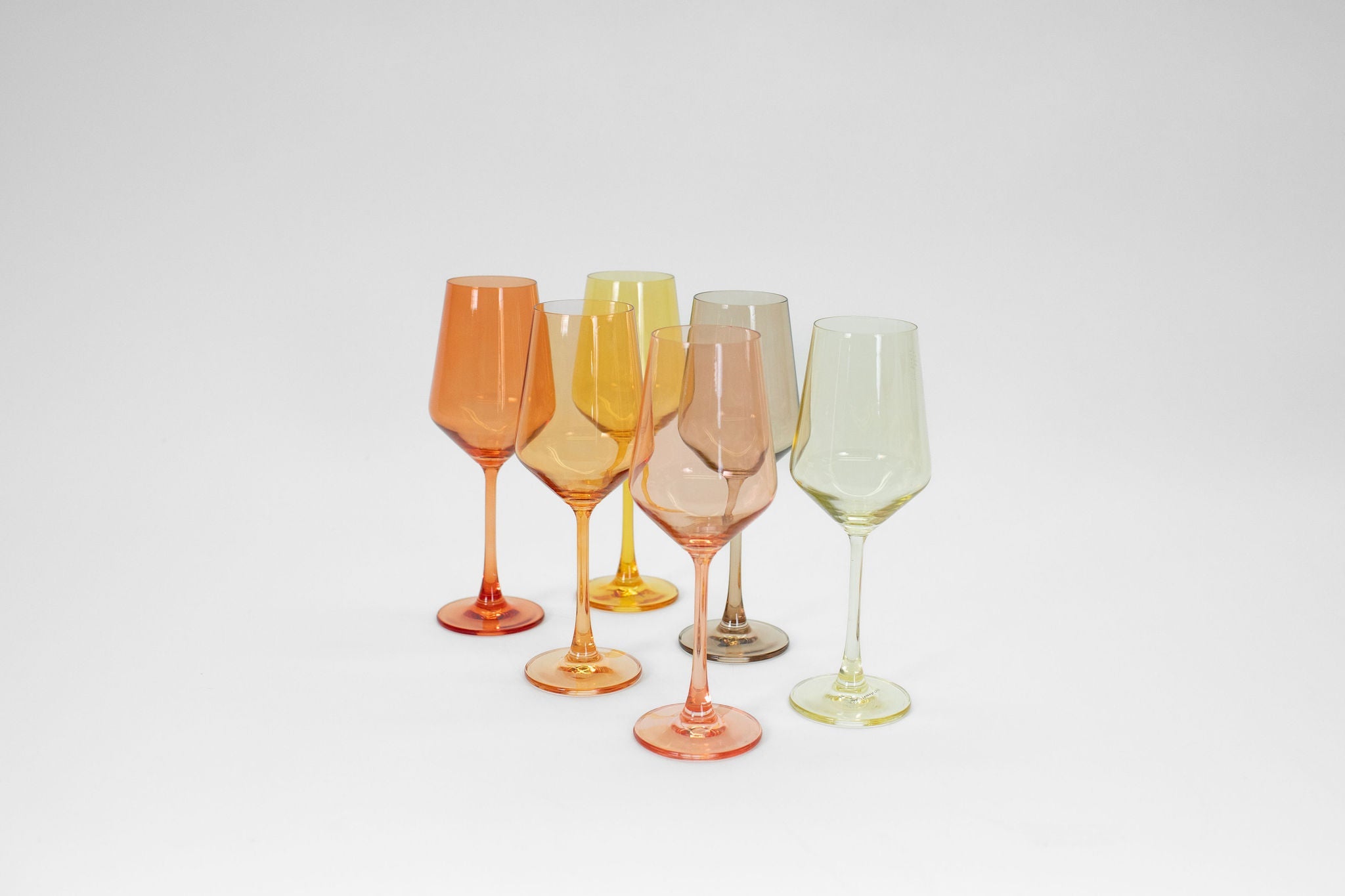 Six stemless wine glasses in a variety of ombré orange and yellow tones arranged together