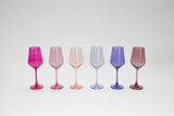 Six translucent colored wine glasses in shades of red, pink, peach, light blue, purple, and rose, arranged in a row against a white background.
