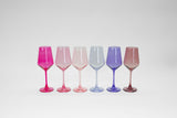 Six stemmed wine glasses arranged in a row showing an ombré gradient from bright pink to dusty rose with varying shades of pink, purple, and blue in between.