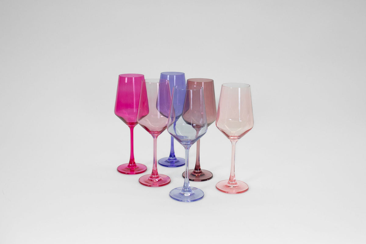 Set of five stemmed wine glasses in varying ombré shades of pink, purple, and blue, arranged in a slight arc on a white background.