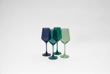 Set of four stemless wine glasses in varying translucent colors including dark blue, teal, and light green, arranged in a group on a white surface.
