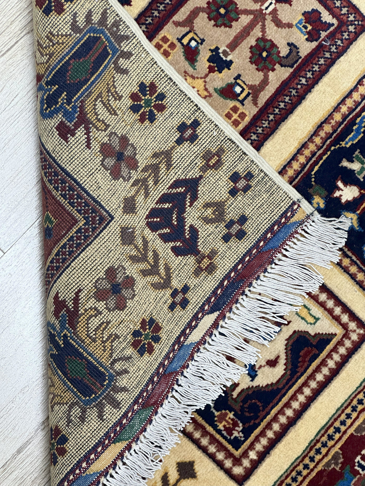 Corner view of a hand-knotted Afghani Bakhteiari wool rug with intricate geometric and floral patterns in beige, brown, navy, and green, showing detailed fringe and texture.