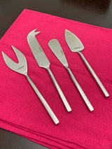 Set of four stainless steel cheese knives with textured handles arranged on a folded red cloth on a dark surface.