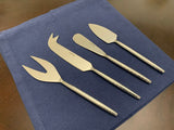Set of four silver stainless steel cheese knives with textured handles displayed on a dark blue cloth, each knife head featuring a distinct shape for different cheese types.