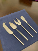 Set of four stainless steel silver cheese knives with distinct blade shapes arranged on a blue cloth atop a wooden surface.