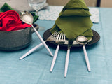 Set of stainless steel flatware with white handles arranged on a blue tablecloth next to green and red folded napkins on dark plates.