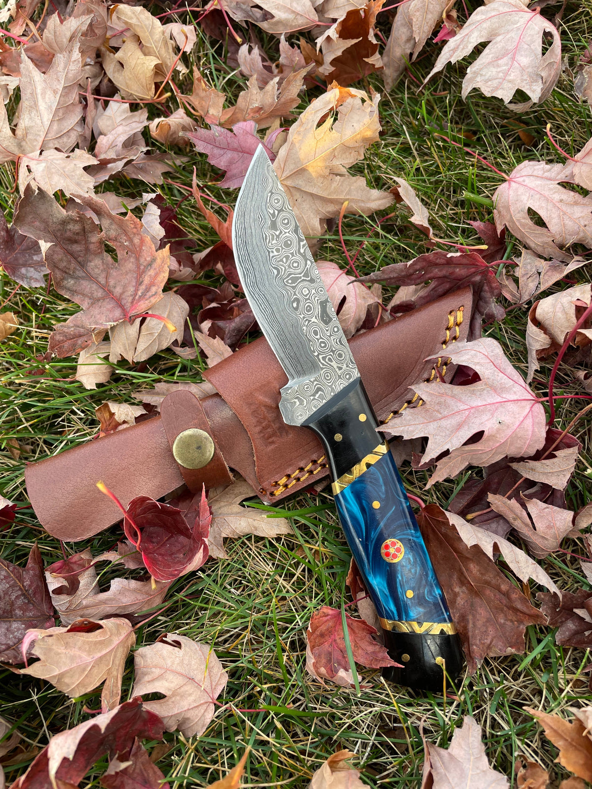 Blue Phantom TK-213 fixed blade knife with blue and black resin handle alongside a leather sheath on a wood surface