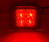 Square LED pod emitting bright red light with four visible circular lenses arranged in a 2x2 grid, housed in a black casing with horizontal ridges on top.