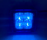 Square LED pod light emitting bright blue light through a clear lens with four circular segments, shown close-up in a dark setting.