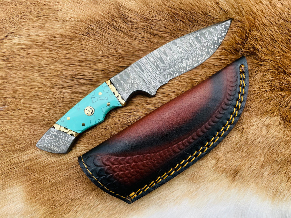 The Azure Fusion Damascus Steel Utility Knife TK-086 showing the patterned Damascus steel blade and turquoise resin handle resting on a textured surface