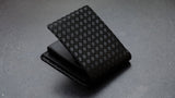 Black folded wallet with a textured checkered pattern on the exterior, resting on a gray surface at an angled view.