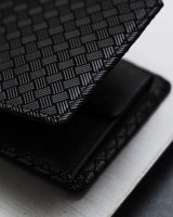 Close-up of a black folded wallet featuring a textured woven pattern on its surface with subtle alternating glossy and matte square grid design.