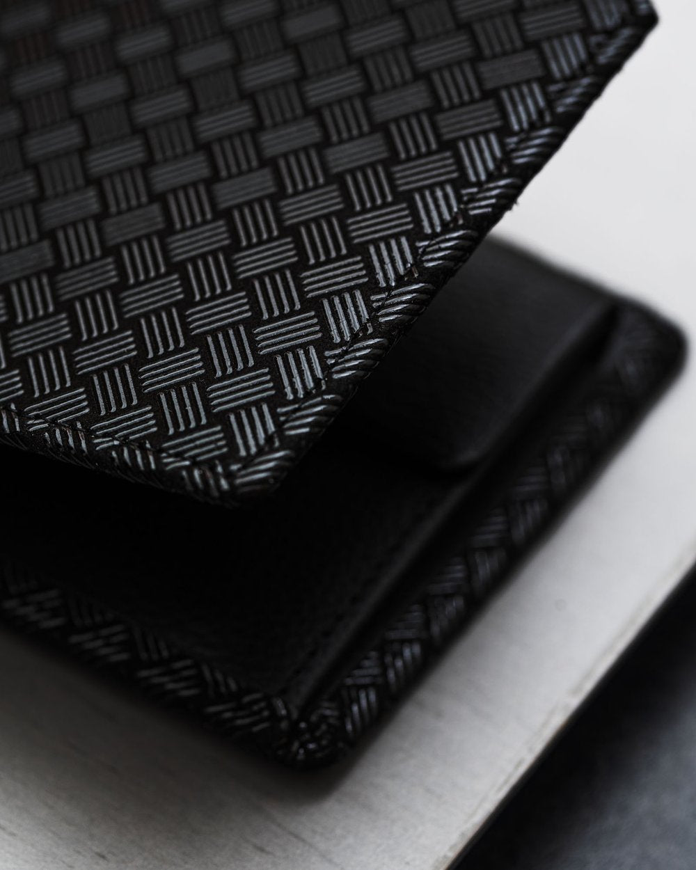 Close-up of a black folded wallet featuring a textured woven pattern on its surface with subtle alternating glossy and matte square grid design.