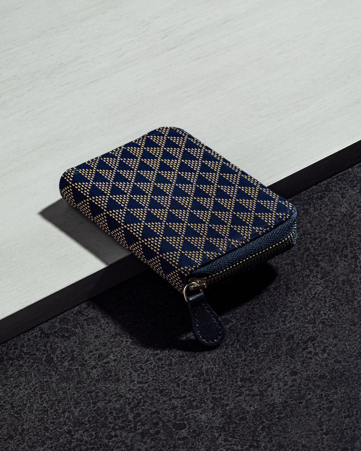 Rectangular coin purse with a navy and beige geometric UROKO pattern, featuring a zipper closure and rounded corners, placed on a two-tone surface.