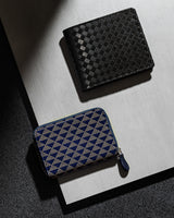 Two compact wallets on a layered surface; top is a black bi-fold with a checkerboard texture, bottom is a navy zip-around with beige geometric triangle pattern.