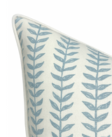 Close-up of a linen pillow cover featuring a repeating vertical blue willow floral pattern on a natural off-white background with white piping along the edges.